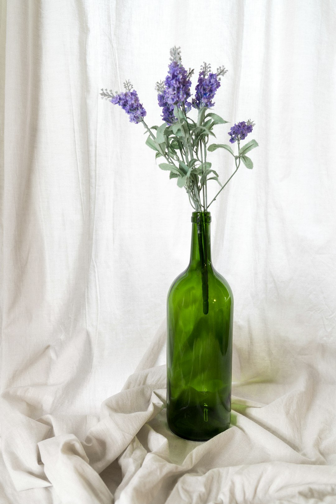 A green glass bottle with lavender among soft neutral tones