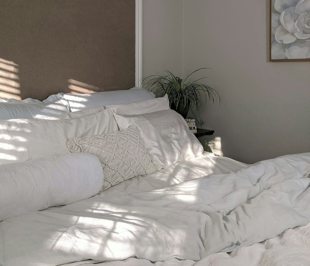 Crisp white bed linen beside a green plant in a calm, quiet room
